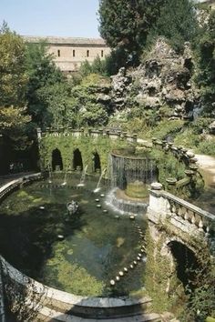 an outdoor fountain surrounded by greenery and stone walls in the middle of a park