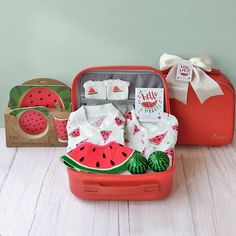 an open suitcase filled with watermelon items on top of a wooden floor next to a box