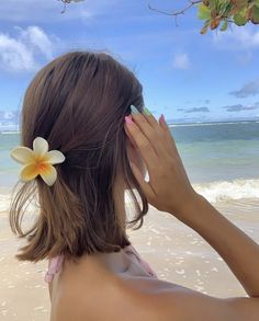 a woman on the beach holding her hand up to her face with a flower in her hair