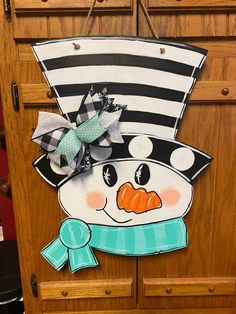 a snowman door hanger with a bow on it's head in front of a wooden cabinet