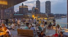 many people are sitting at tables on the roof of a building with city lights in the background