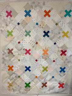 a quilt made with different colored squares and crosses on it's sides, hanging from a wall