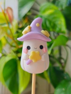 a close up of a cake on a stick near a potted plant with leaves in the background