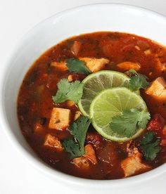 a white bowl filled with chicken and tortilla soup next to a lime slice