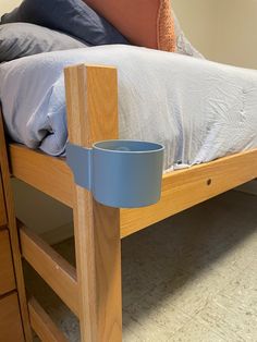 a wooden bed frame with a blue plastic cup on the bottom and an orange pillow behind it