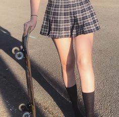 a woman in plaid skirt holding a skateboard