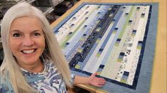 a woman smiling next to a quilt on a table