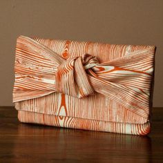 an orange and white clutch bag with a bow on the front sitting on a wooden table