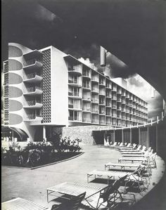 an old black and white photo of a building with lounge chairs in the foreground