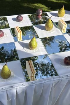 several pears and cheese on a checkerboard table with trees in the background