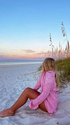 a woman sitting on top of a sandy beach next to tall grass and sea oats