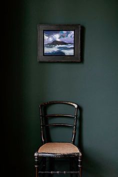 a chair sitting next to a green wall with a painting on the wall above it