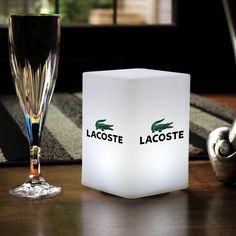 a lit up wine glass next to a lamp on a table with the lacoste logo