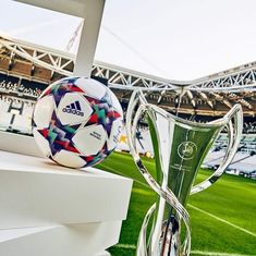 a soccer ball sitting on top of a white pedestal next to a trophy in front of a stadium