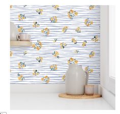 a white vase sitting on top of a counter next to a wall with yellow flowers