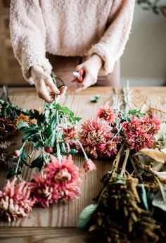 a woman arranging flowers on a table with other dried flowers in front of her,