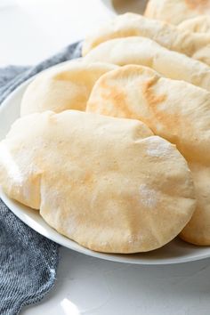 several uncooked pita breads on a white plate next to a blue towel