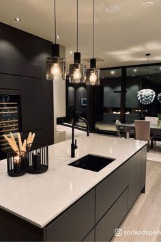 a modern kitchen with black cabinets and white counter tops is lit by pendant lights that hang from the ceiling