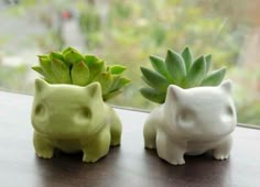 two ceramic animals sitting next to each other on a window sill with plants in the background