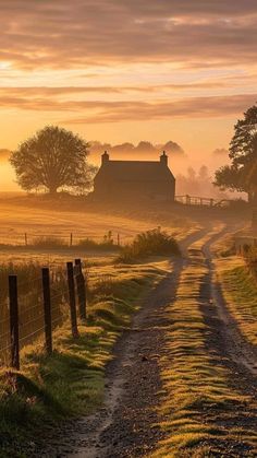 the sun is setting on a farm road with a barn in the distance and fog covering the sky