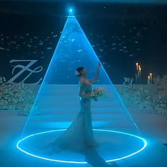 a woman in a blue dress is standing on a stage with an illuminated pyramid behind her