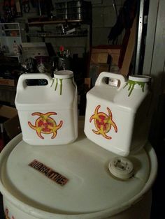 two white containers with yellow and red designs sitting on top of a metal barrel in a garage