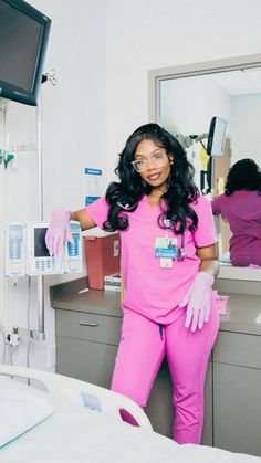 a woman in pink scrubs is standing next to a hospital bed and looking at the camera