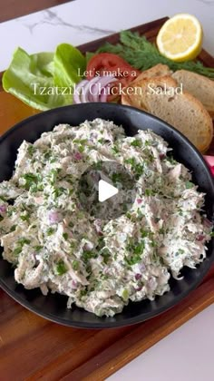 a bowl filled with chicken salad on top of a wooden cutting board next to bread