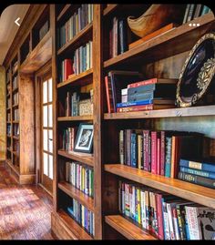 a room filled with lots of books on top of wooden book shelves next to a window