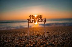 a cake topper that says happy birthday on the beach at sunset with waves in the background