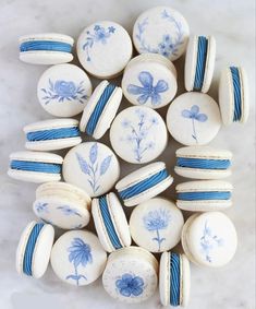 blue and white macaroons are arranged on a marble surface, with flowers painted on them