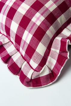 a red and white checkered pillow with ruffles on the bottom, sitting on a white surface