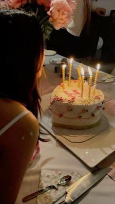 a woman sitting in front of a cake with lit candles