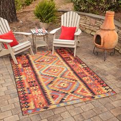 two chairs sitting on top of a colorful rug next to a fire place in the middle of a yard