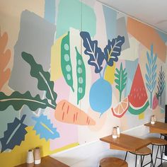 a colorful mural in a restaurant with wooden tables and stools next to it on the wall