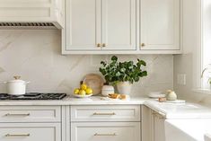 a kitchen with white cabinets and marble counter tops, potted plants on the stove