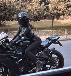 a woman in black riding on the back of a motorcycle