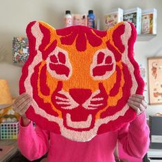 a woman holding up a red and orange tiger rug in the shape of a cat