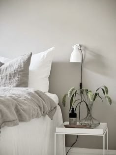 a white bed sitting next to a night stand with two plants on top of it