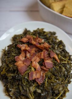 a white plate topped with spinach and bacon next to a bowl of cornbread