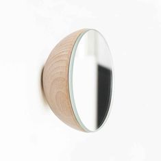 a round mirror mounted to the side of a wall next to a wooden object with a white background