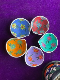 four colorful bowls sitting next to each other on a purple tablecloth covered floor, with one empty bowl in the middle