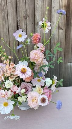 a vase filled with lots of flowers on top of a wooden table next to a fence