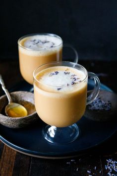 two glasses filled with liquid sitting on top of a blue plate next to spoons