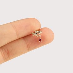 a person's hand holding a tiny gold bird ring with a red stone on it