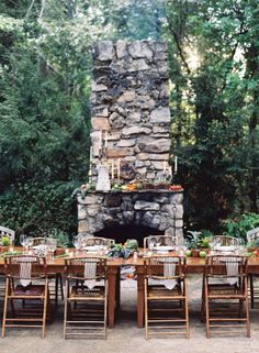 an outdoor dining table with chairs around it and a fire place in the middle surrounded by trees