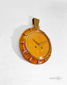 an orange watch with gold hands on a white surface and shadow from the clock's face