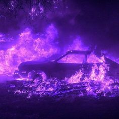 a car on fire in the dark with purple flames around it and trees behind it