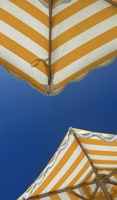 two yellow and white striped umbrellas against a blue sky