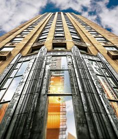 a tall building with lots of windows on the top and bottom floors, against a blue sky with clouds